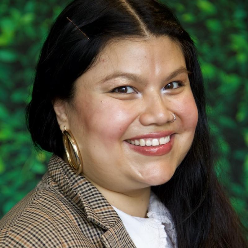 A photo of Brenda Barrios wearing a striped blazer and white shirt with a green background.