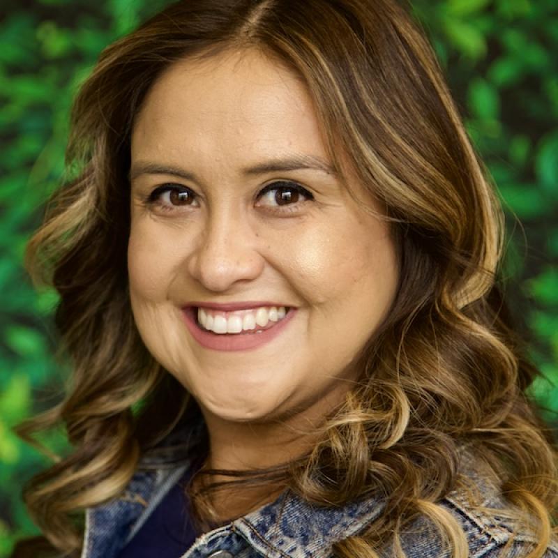 A photo of Karina Garcia wearing a jean jacket with a green background.